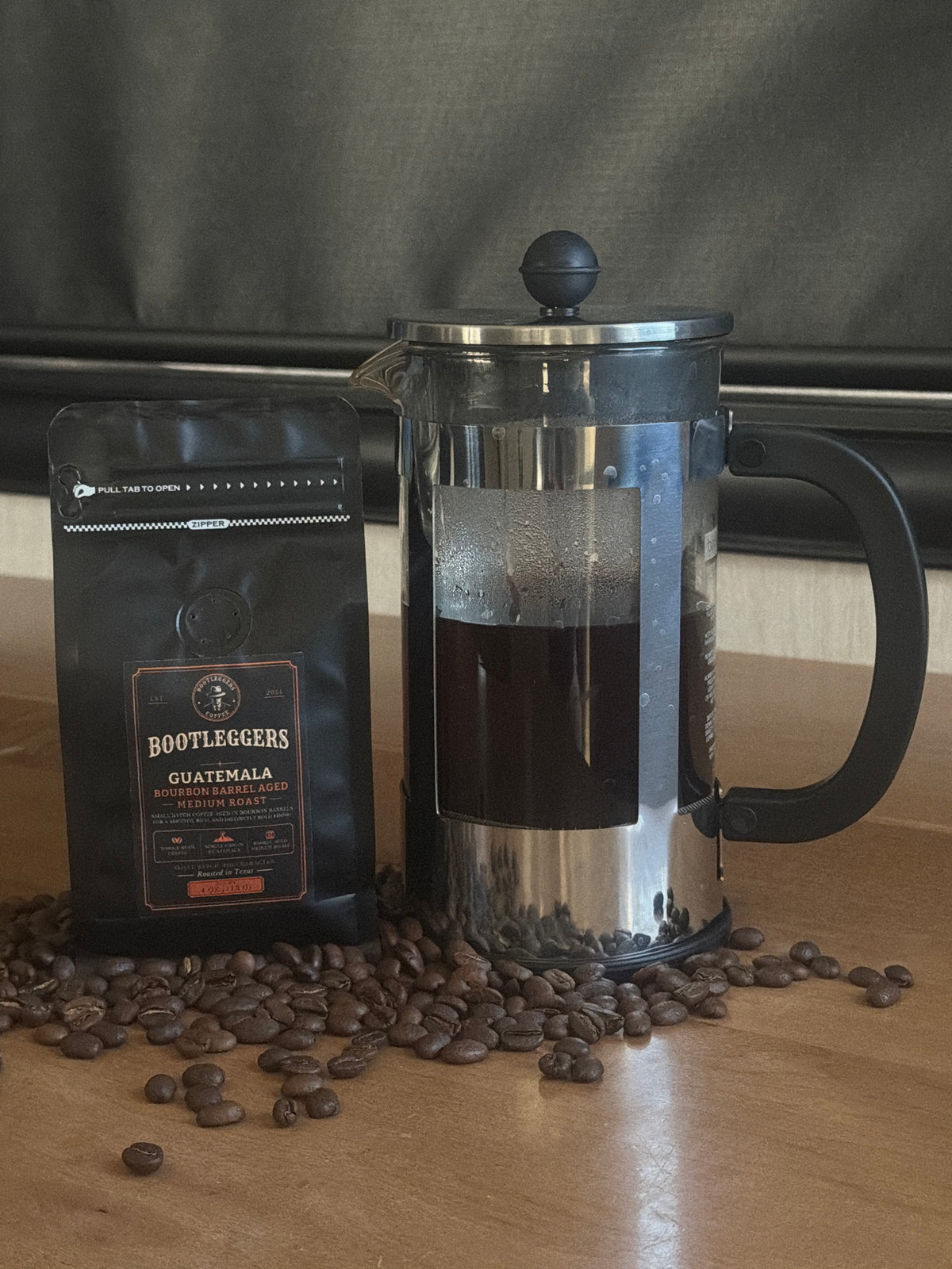 Optional add-on: 4 oz bag of Bootleggers Bourbon Barrel Aged Guatemala Medium Roast next to a French press of brewed coffee